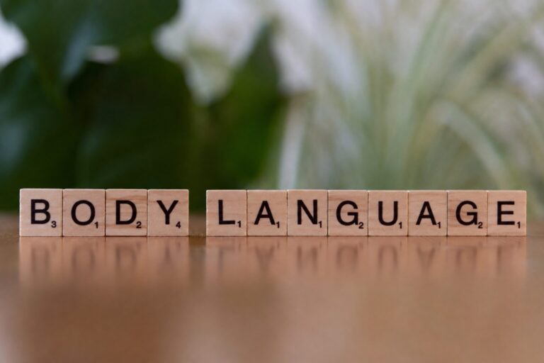 Fa Scrabble-kockákból kirakott BODY LANGUAGE felirat zöld növény előtt, a nonverbális kommunikáció témáját szimbolizálva